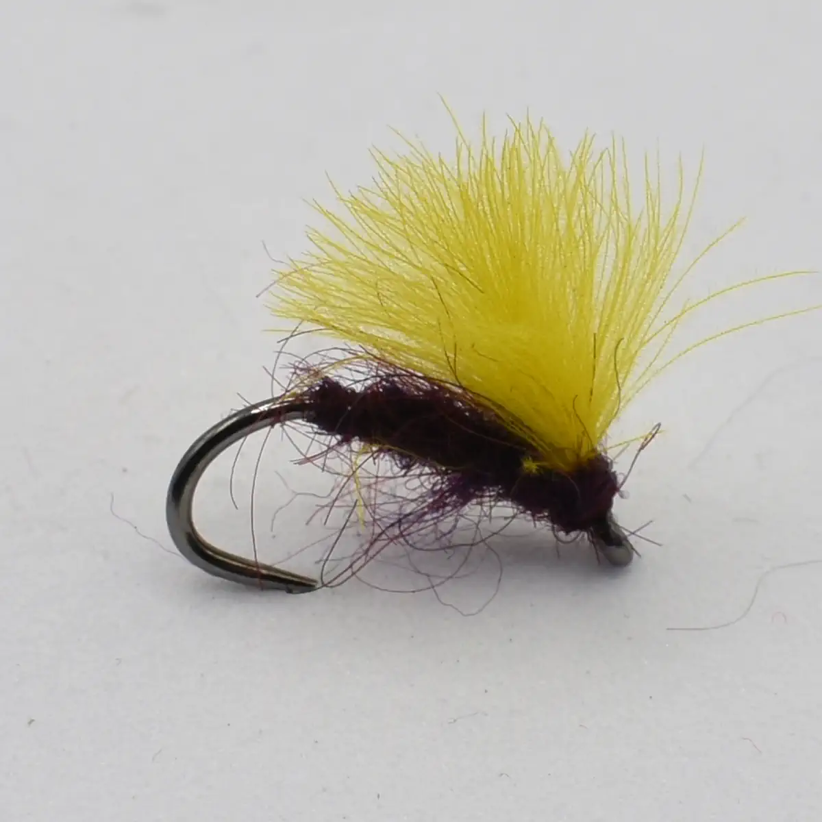 Yellow fluffy fishing fly tied to a small curved hook, an artificial lure for fly fishing.