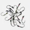 Assorted fishing hooks scattered on a white surface, black with colored bands near the eye and barb exposed.