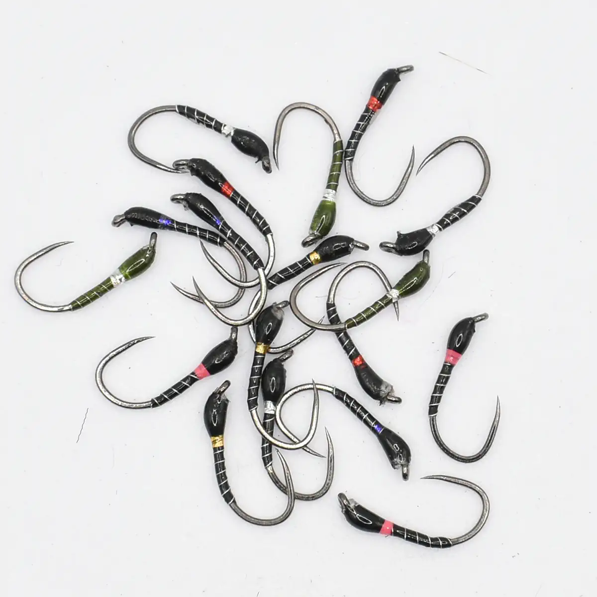 Assorted fishing hooks scattered on a white surface, black with colored bands near the eye and barb exposed.