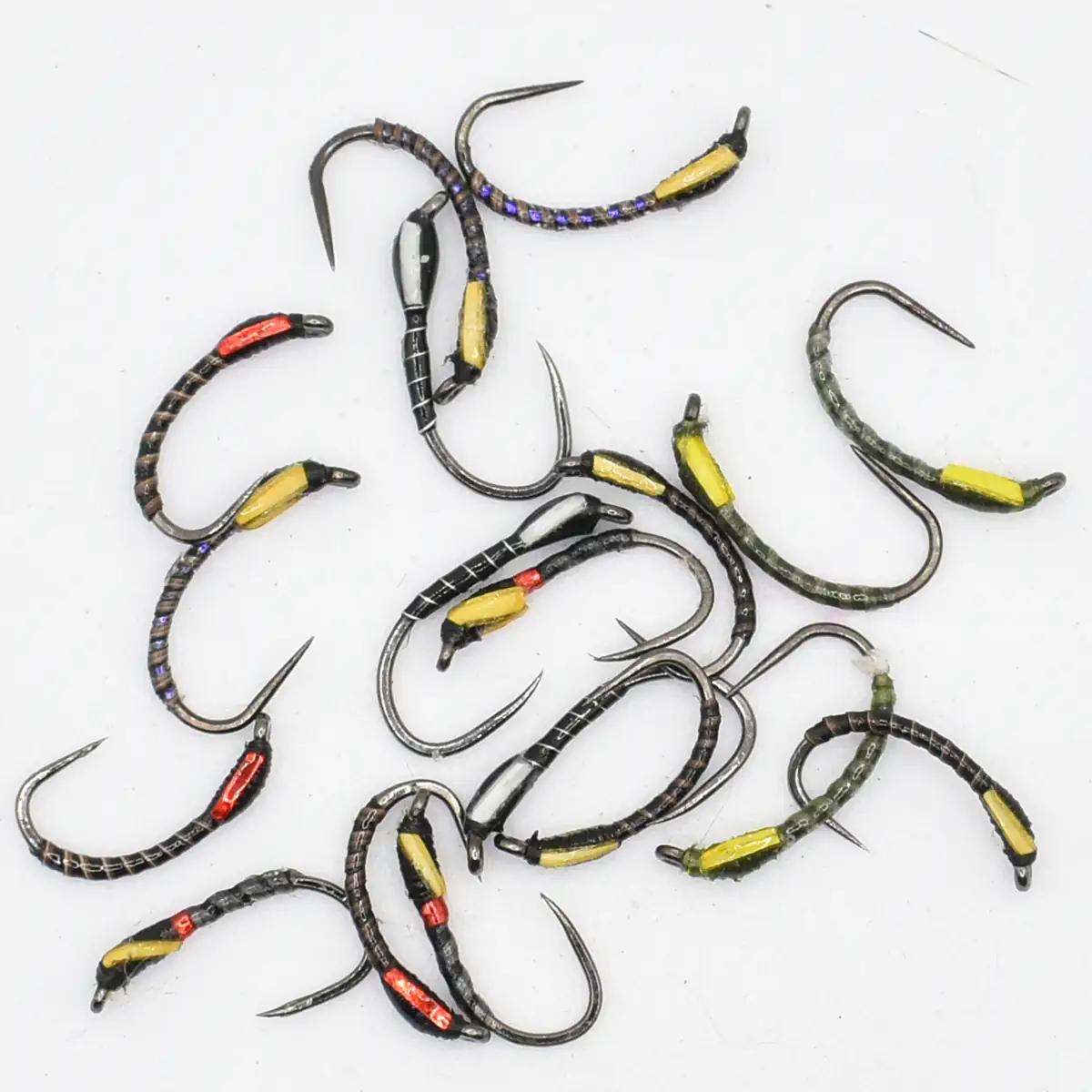Assorted curved fishing hooks with colorful bead wraps (yellow, red, purple) scattered on a white surface.