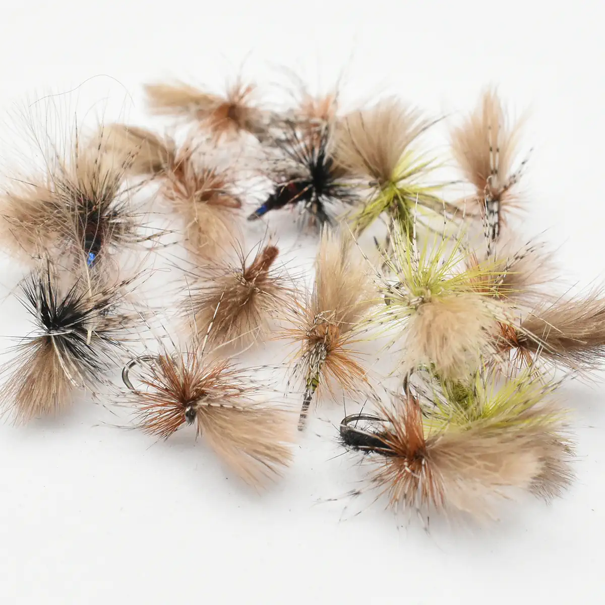 Assorted fuzzy fishing flies with feather wings laid on a white background, used for fly fishing.