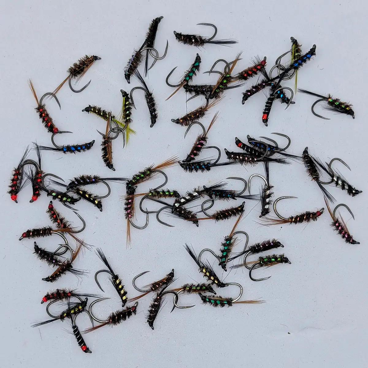 Assorted bead-head fishing flies with colorful bodies scattered on a light surface.