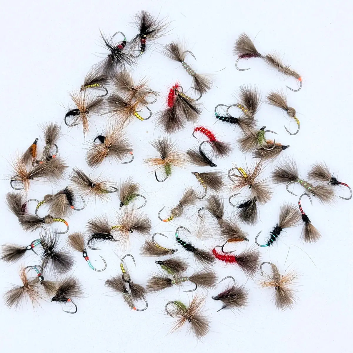 Assortment of fishing flies with fluffy tails and colorful beads laid on a white background, ready for tying or use in fly fishing