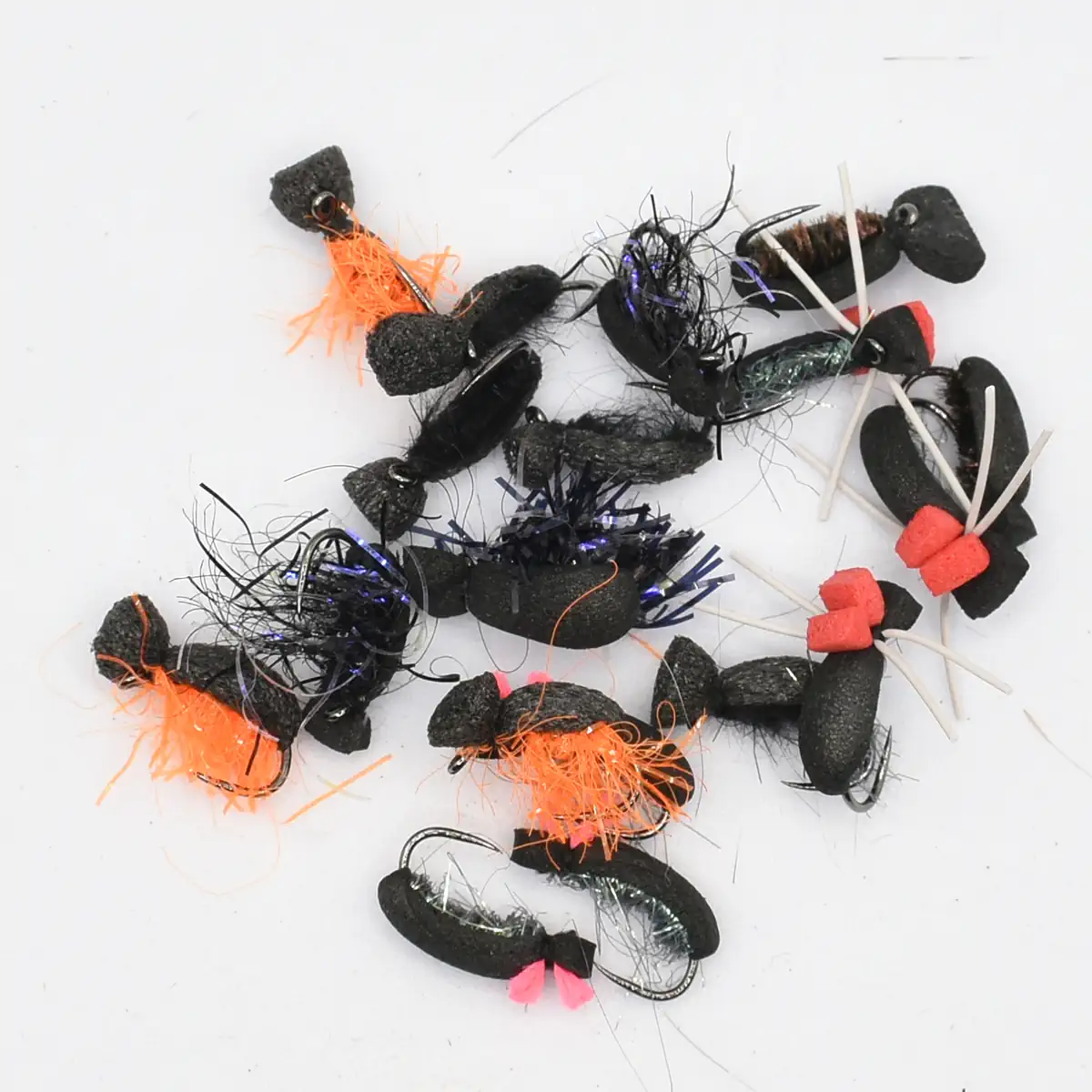 Assorted fishing lures and jigs with black foam bodies and orange accents scattered on a white surface.
