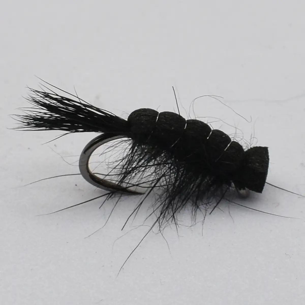 Close-up of a black fuzzy fishing fly tied to a curved hook with long hair fibers protruding from the body.