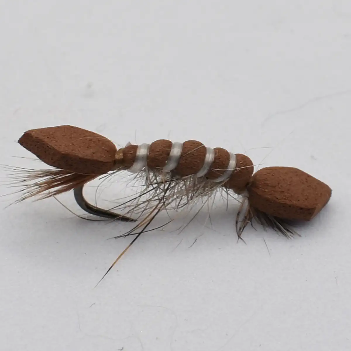 Brown bead-headed fishing lure with fur tail and white thread wraps around a hooked shaft (bead nymph style).