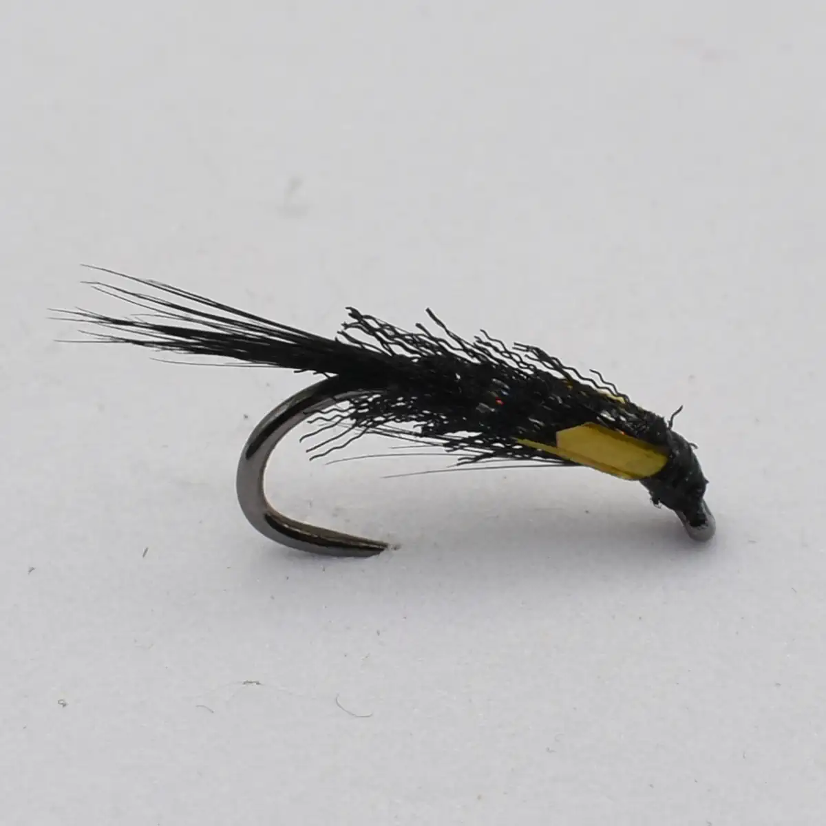 Black streamer fishing fly with long feather tails and yellow tag on a curved hook (fly fishing lure)