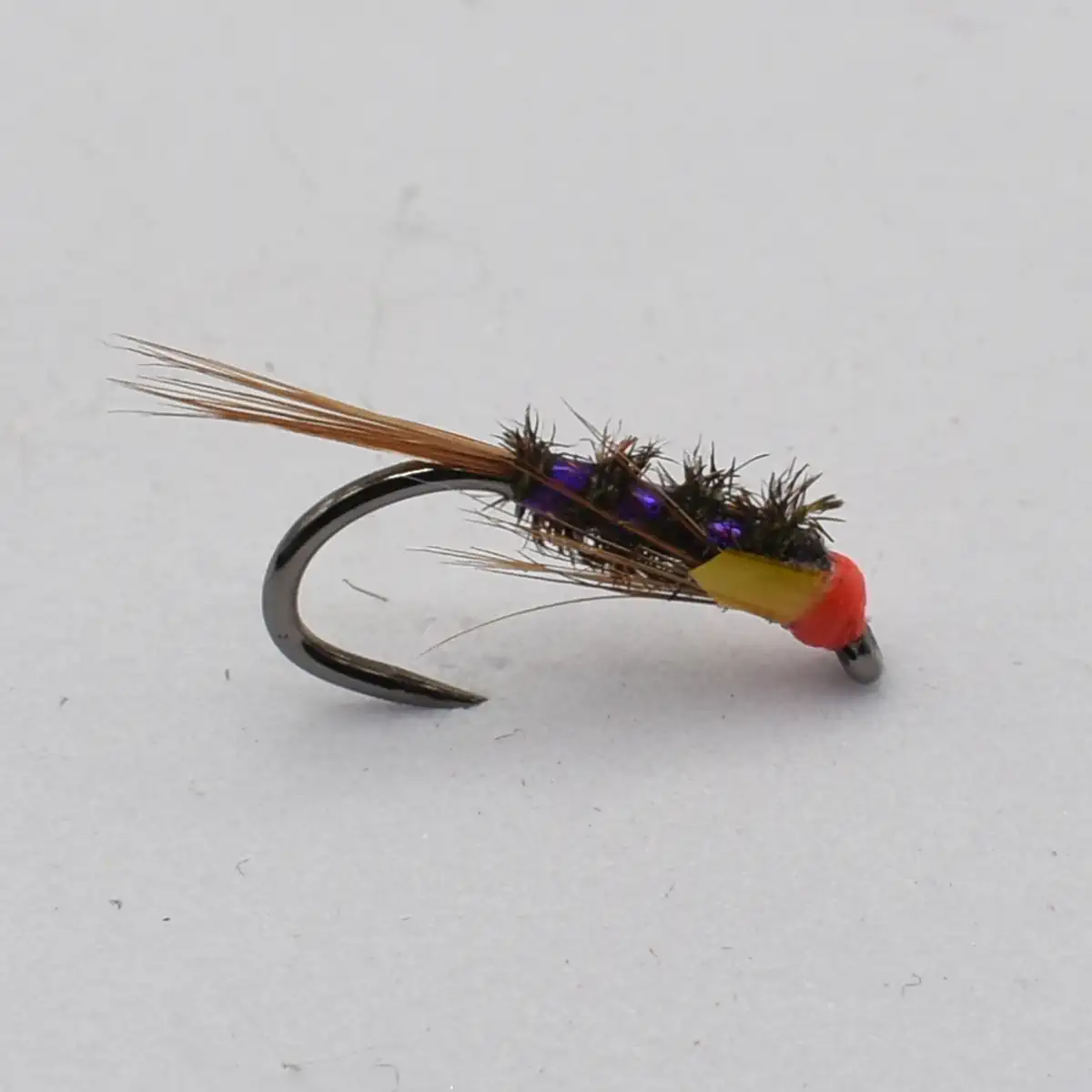 Close-up of a fishing fly lure with a curved metal hook, brown tail feathers, black fuzzy body with purple beads, and a yellow body with a red head.