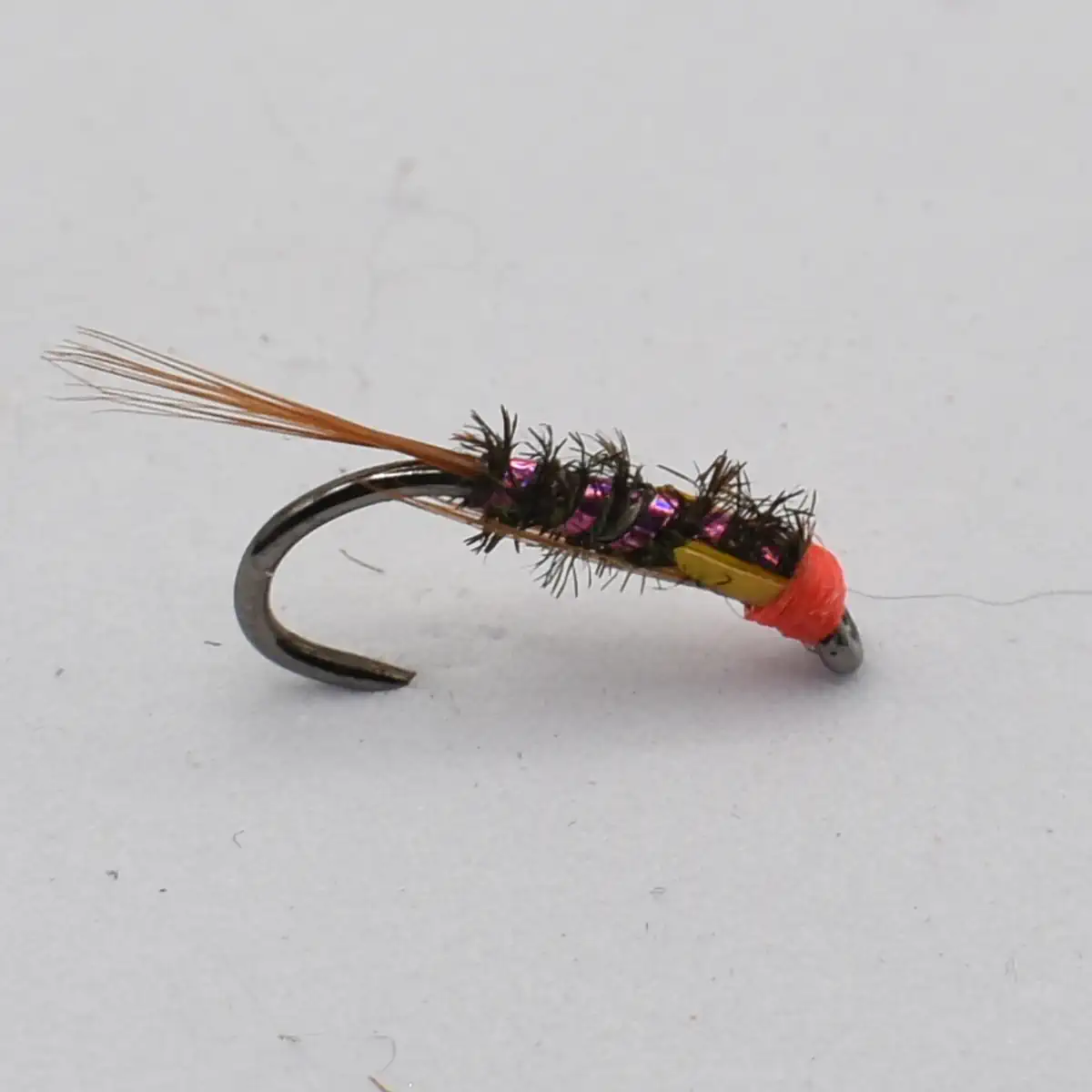 Close-up of a fly fishing lure: curved hook with a black fuzzy body, pink bead accents, orange tail, and a red head external to the eyepoint.