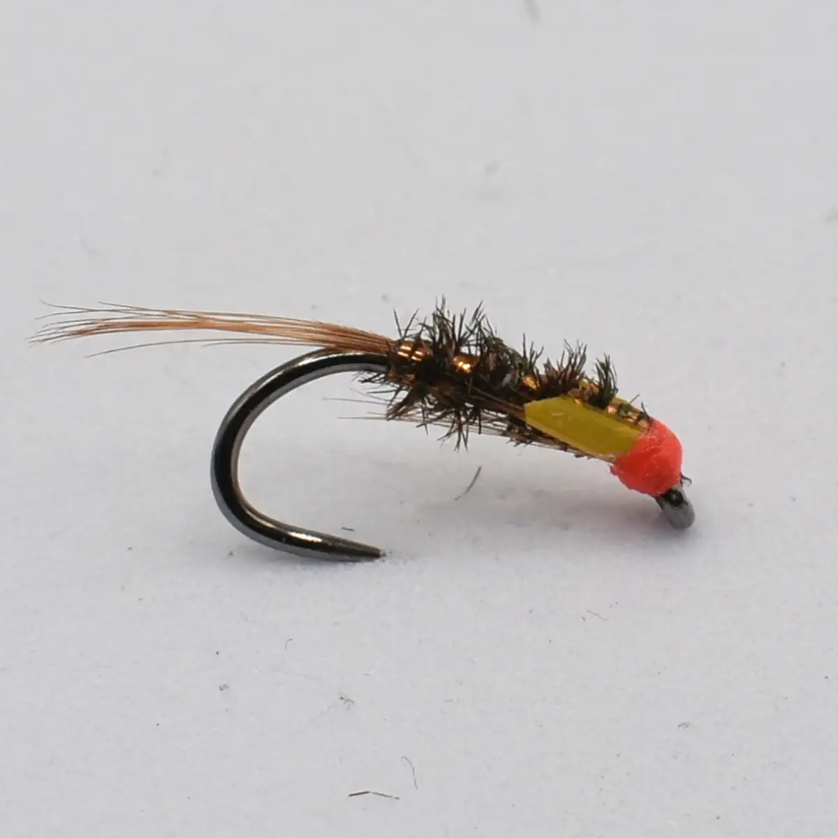 A black and brown fishing fly with a bright red head on a curved hook, used for fly fishing.