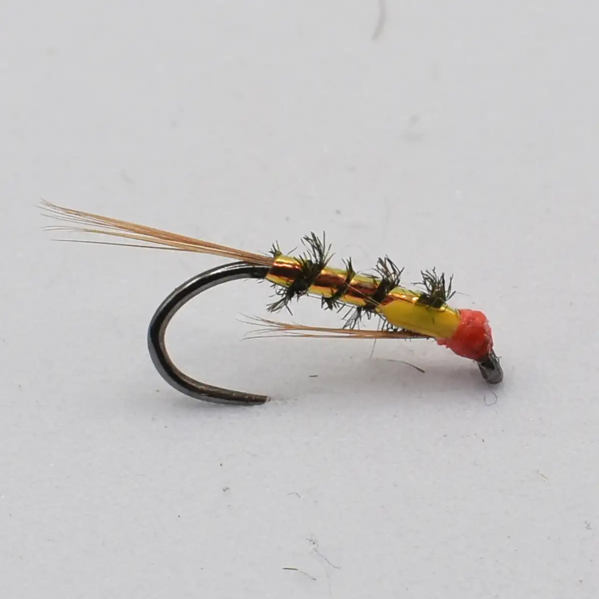 Close-up of a colorful fishing fly lure with an orange-yellow body and black hackle on a curved hook.