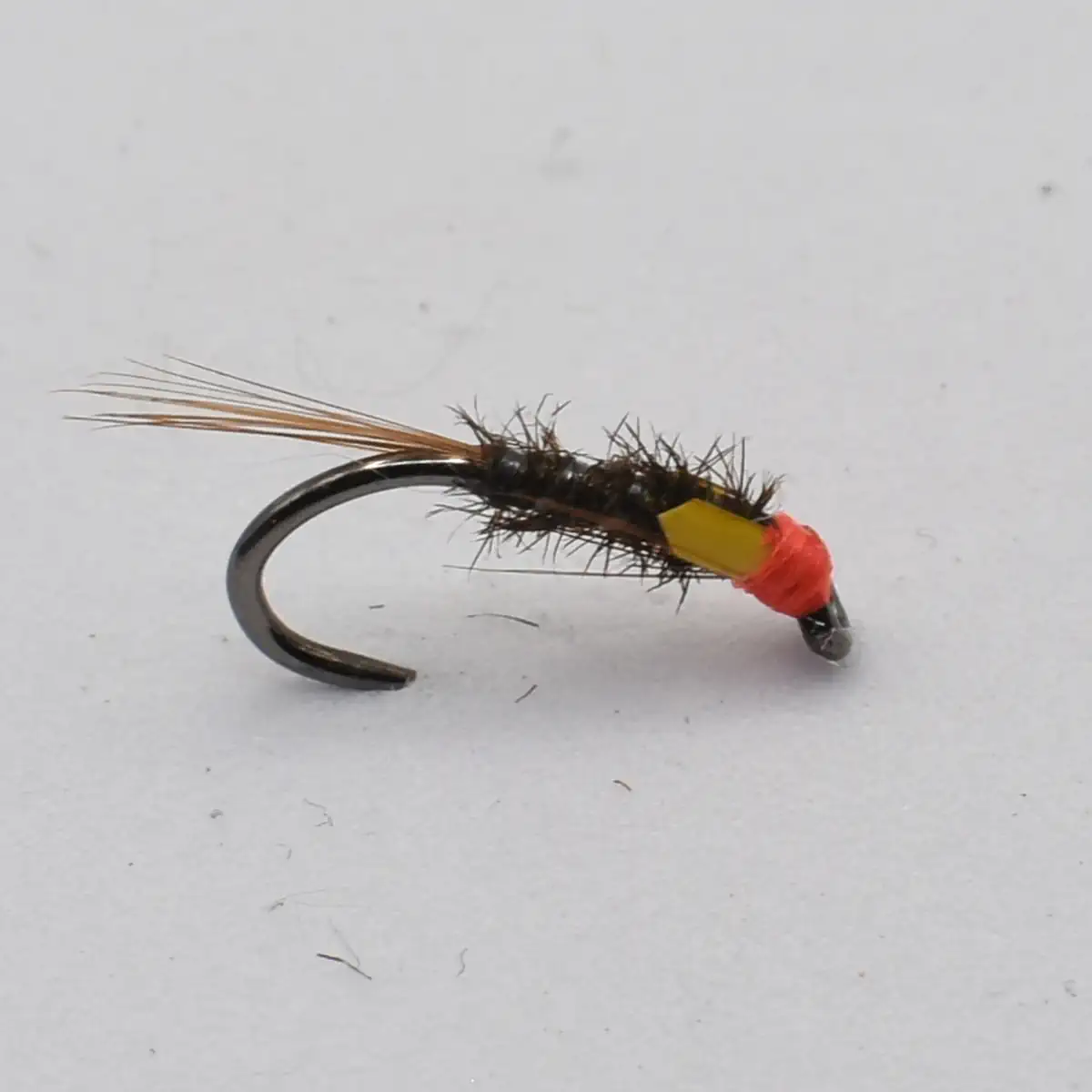 Artificial fishing fly lure: black hook wrapped in hairy brown body with orange head and yellow neck, used for fly fishing