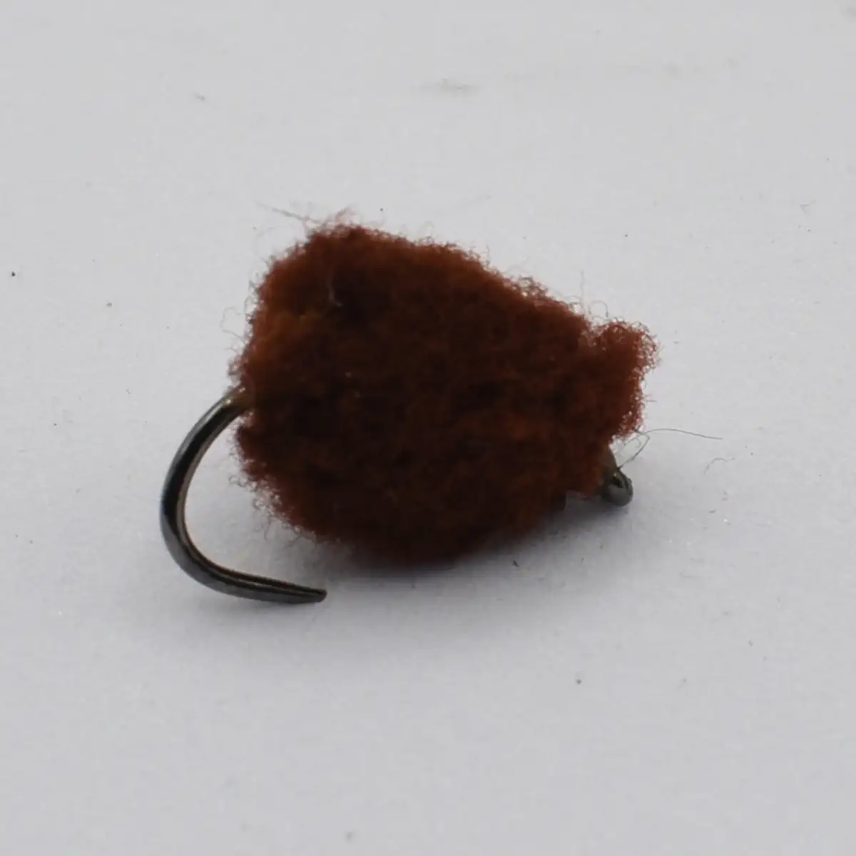 Brown fuzzy fishing lure with a curved hook, resembling a pom-pom jig.
