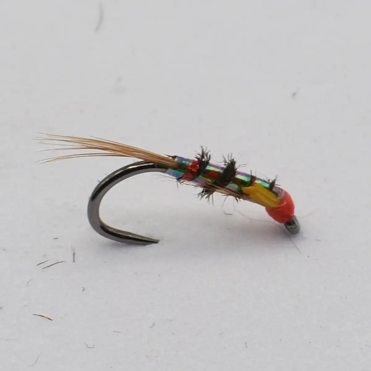 A colorful fishing fly attached to a curved metal hook, with bright green, red, and gold strands and a wispy tan tail.