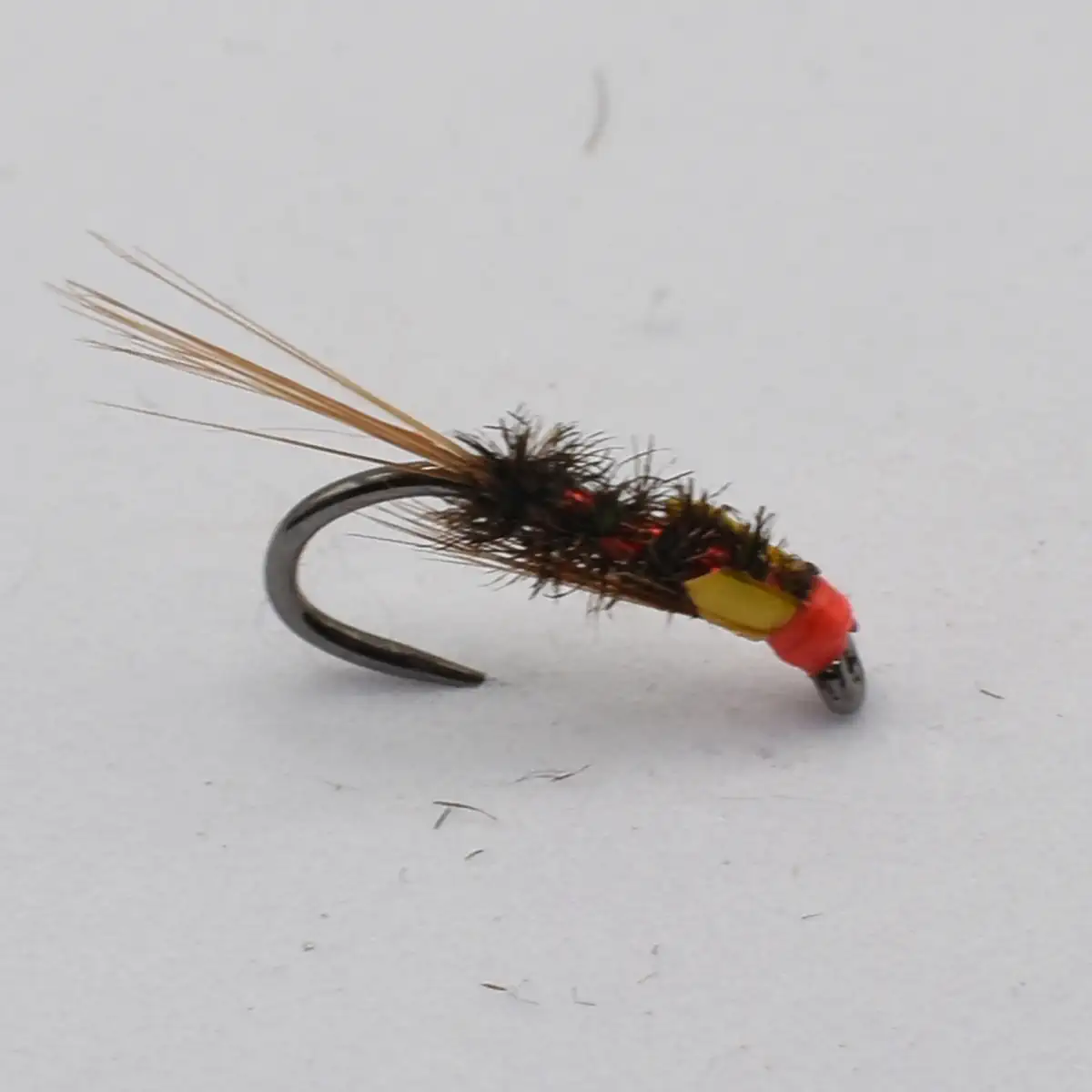 A fishing fly with a dark, fuzzy body, orange head, and long beige tail feathers on a curved hook (tied lure).
