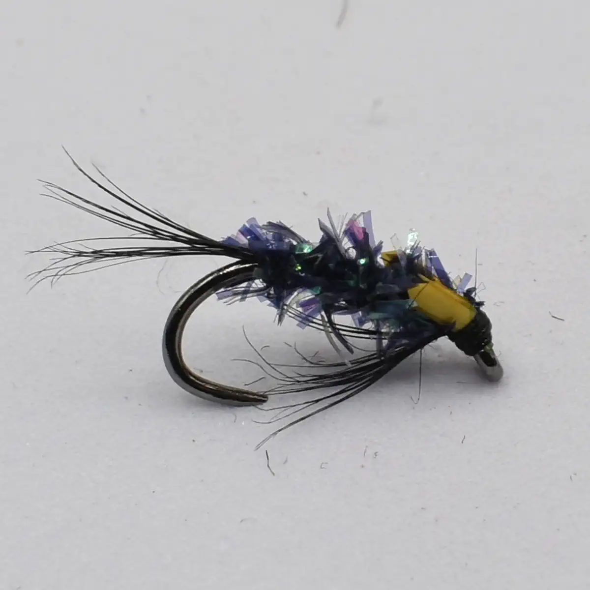 Close-up of a metallic blue and purple tinsel fishing fly tied to a hook with long black tail fibers.