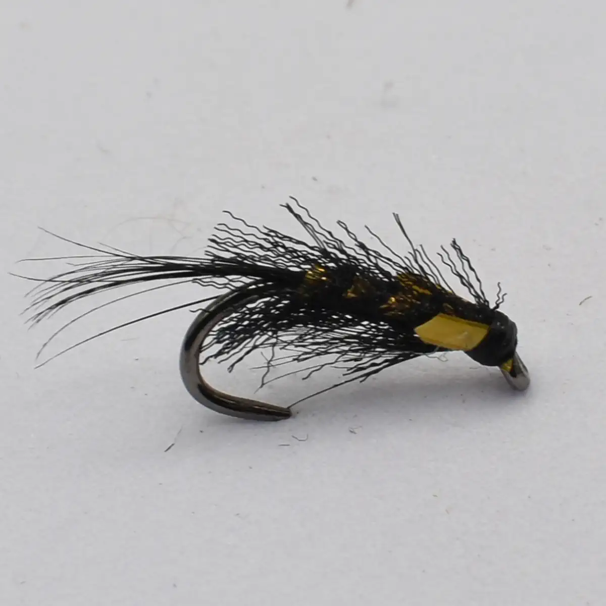 Black, feathered fishing fly with wispy tails and yellow-taped head, used for trout fishing