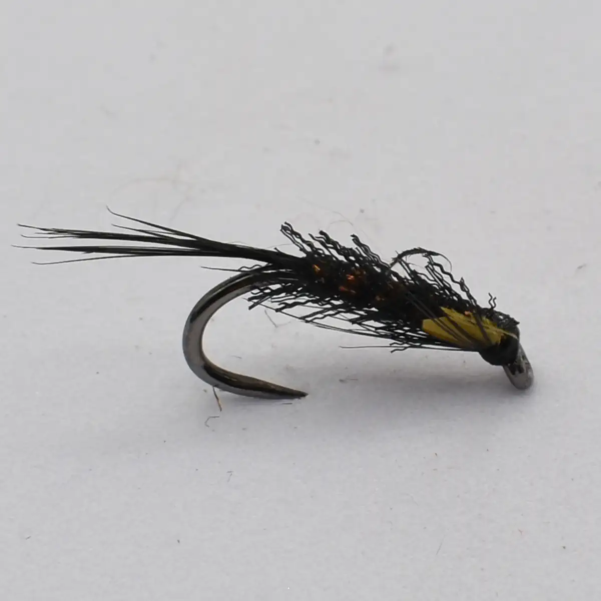 Dry fishing fly lure with black feather hackle and yellow abdomen on a curved hook, isolated on white background