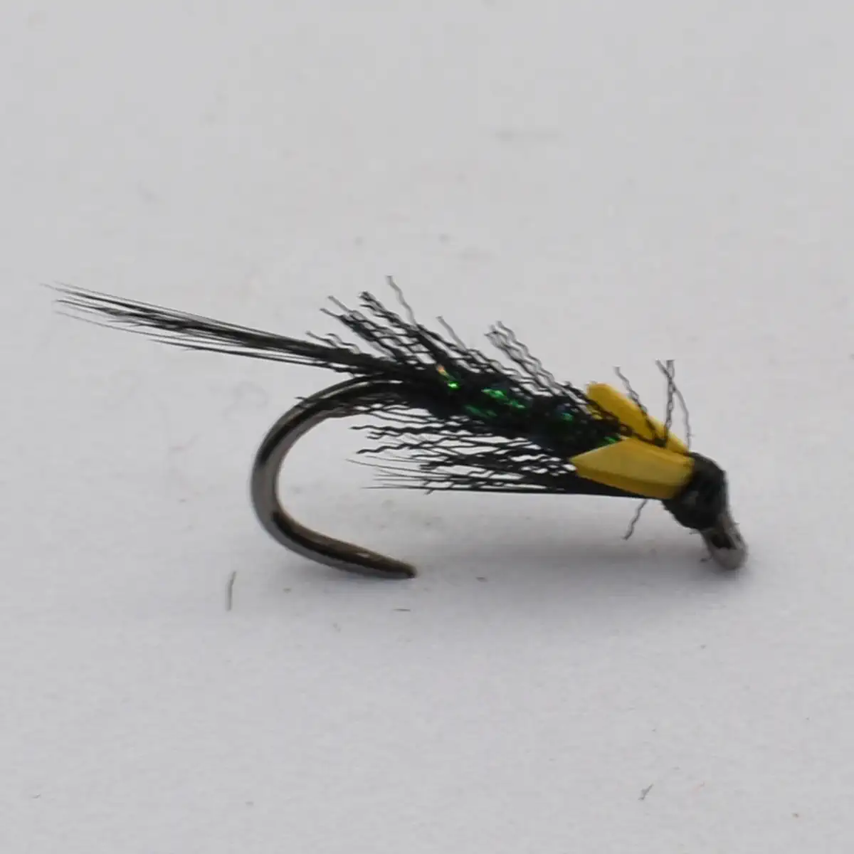 Fly fishing lure with a black feathered body, yellow legs/wings, and a green bead head on a curved hook intent for trout fishing