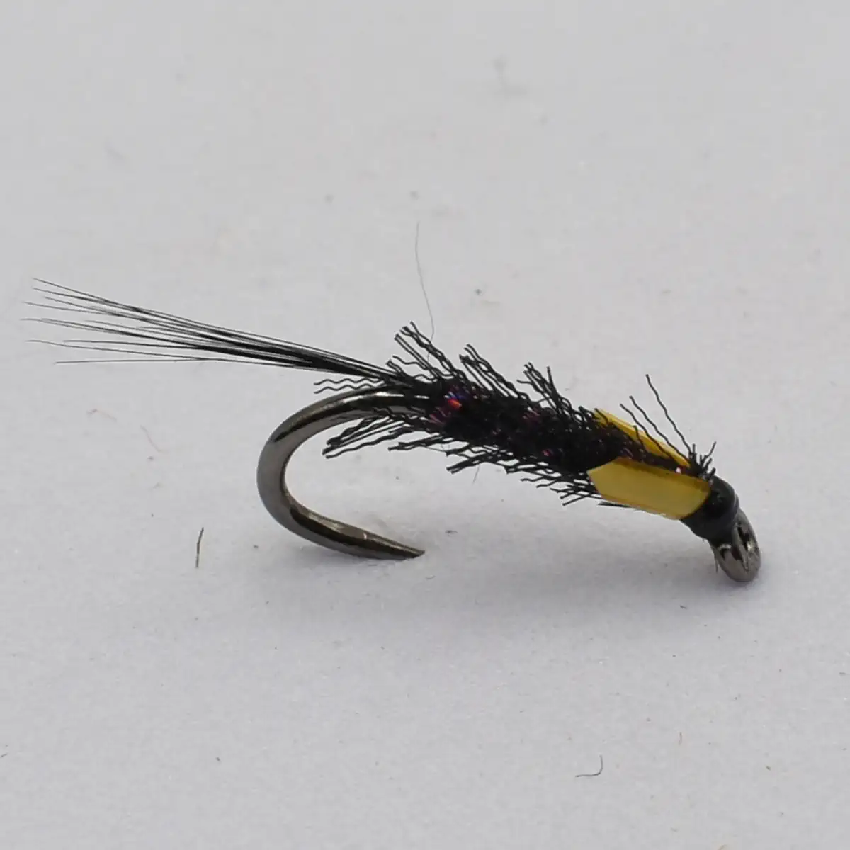 Fly fishing lure with a dark feathered body and yellow segment on a curved hook