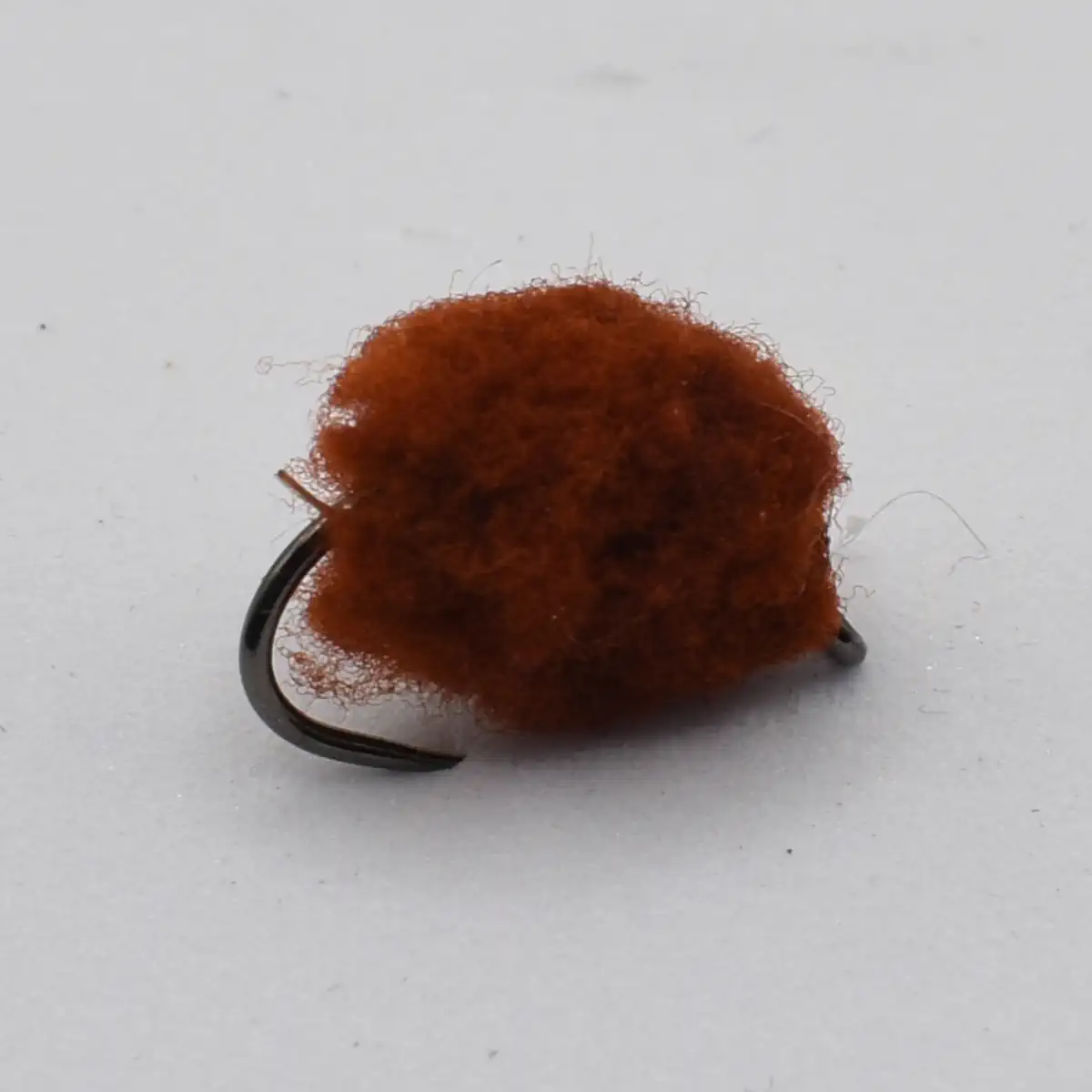 Brown fuzzy pom-pom fishing lure on a curved black hook, viewed close-up