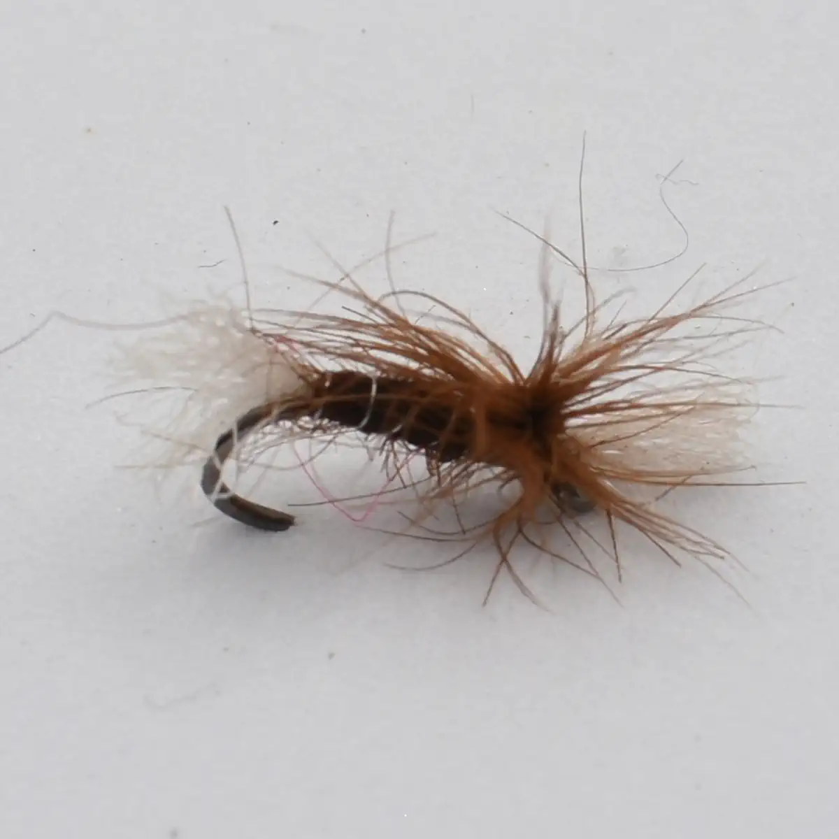 Close-up of a brown and tan fishing fly tied to a curved hook, with fluffy hackle fibers extending outward for lure