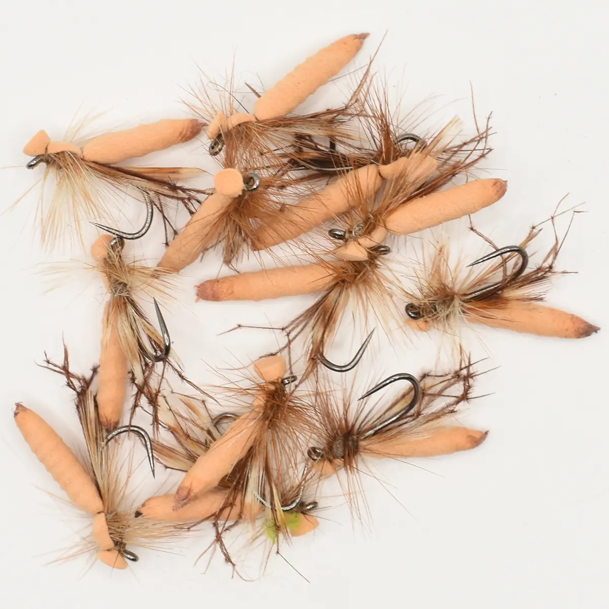 Collection of peach-brown feathered fishing flies with hooks on a white background, ready for tying or use in fly fishing.