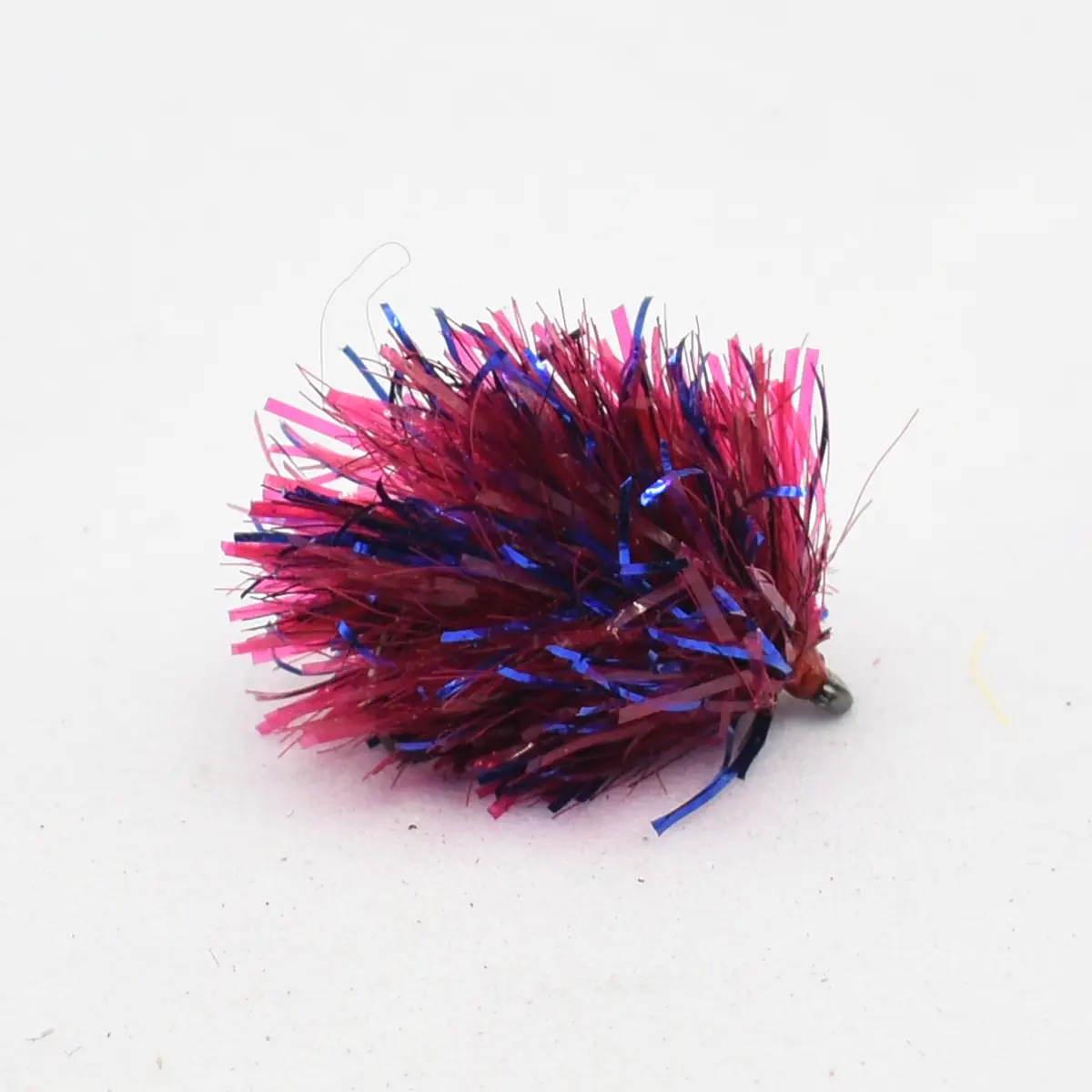 Red and blue tinsel fishing jig with metallic strands and a small hook end on a light background