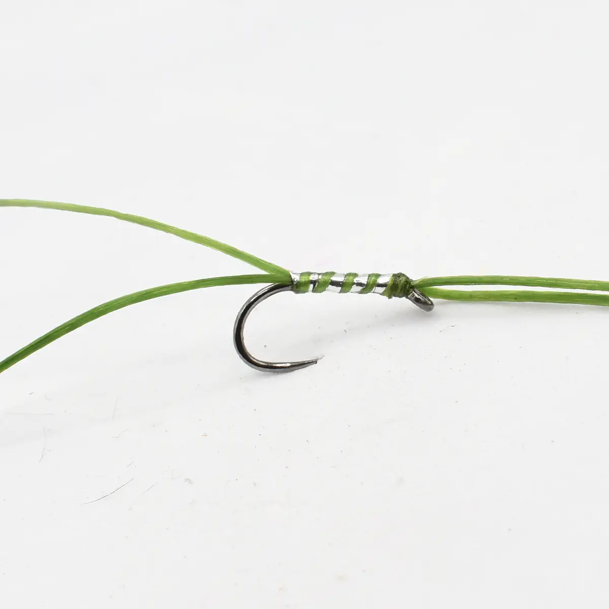 Close-up of a metal fishing hook tied to a green line with thread wraps around the eyelet edge.