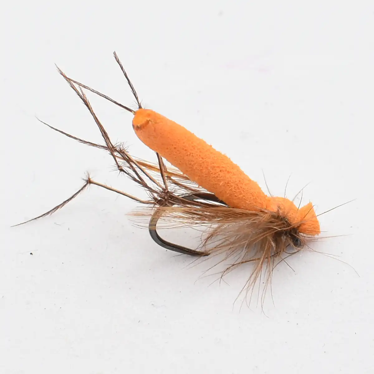 Orange fuzzy fly fishing lure with a curved hook and brown feather tail, used for trout fishing.