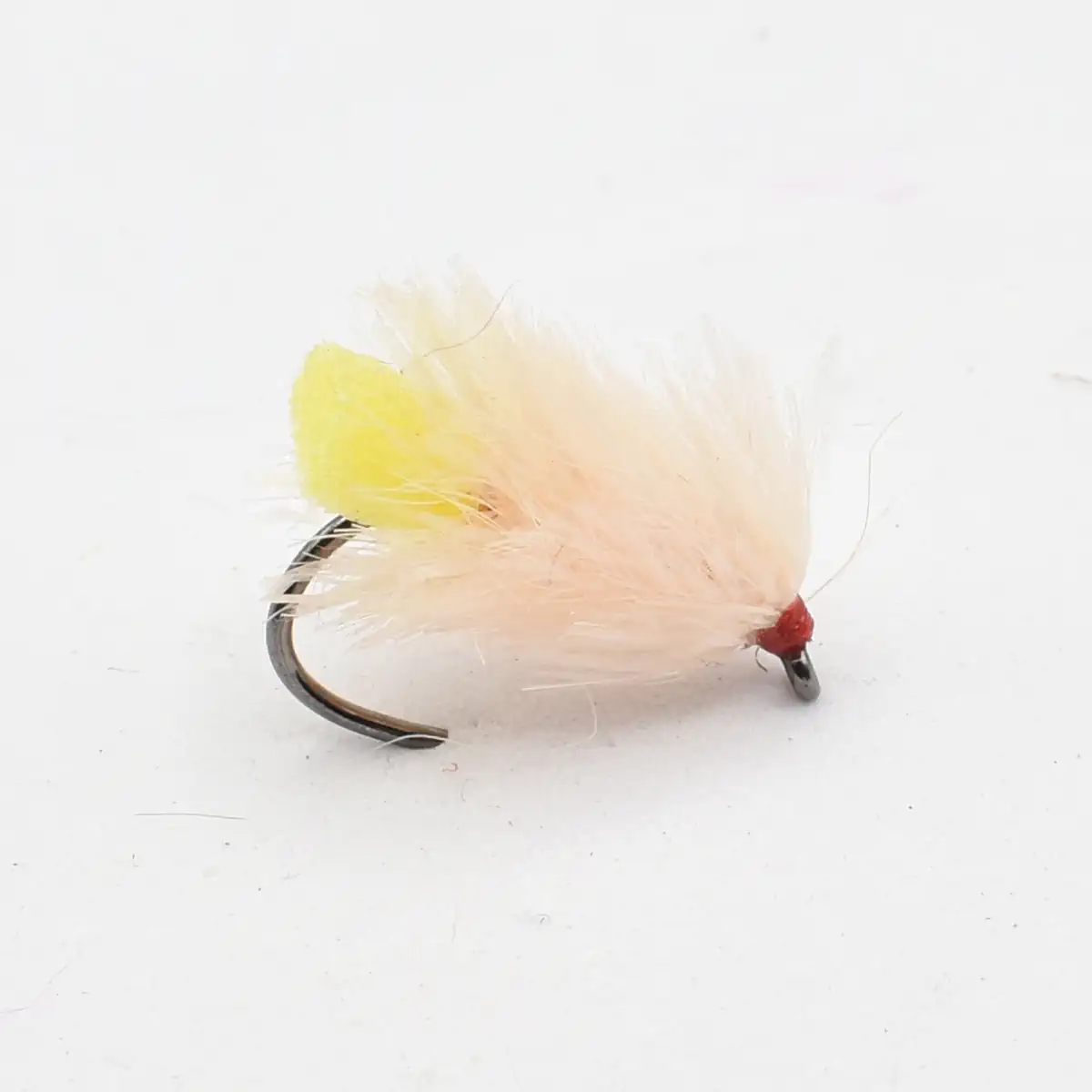 Close-up of a pale pink feather fishing fly with a yellow tail and red bead head on a curved hook.