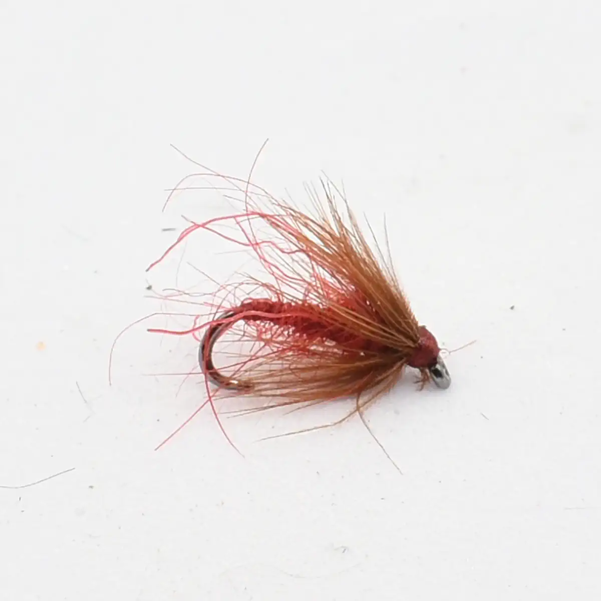 A red-brown fishing fly with a curved hook and wispy hair-like tusks for a lure used in fly fishing.