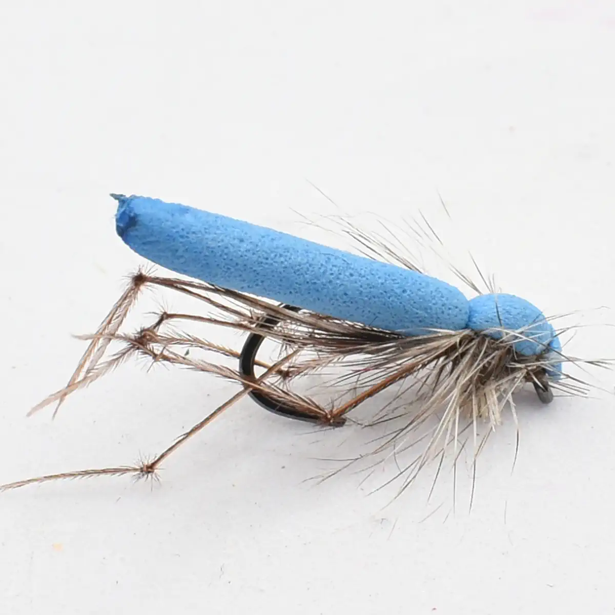Blue foam-bodied fishing lure with brown feathered tail and hooks on a white background