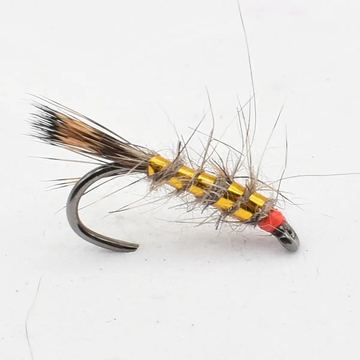 Close-up of a fly fishing lure: curved hook with a segmented yellow body, gray fur, and a red head.