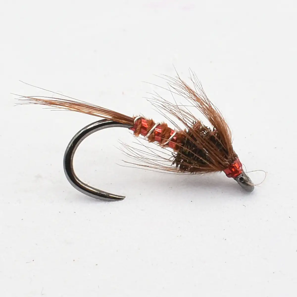 Close-up of a brown/red fishing fly tied on a curved hook, with red thread wraps and brown hackle feathers, used for fly fishing.