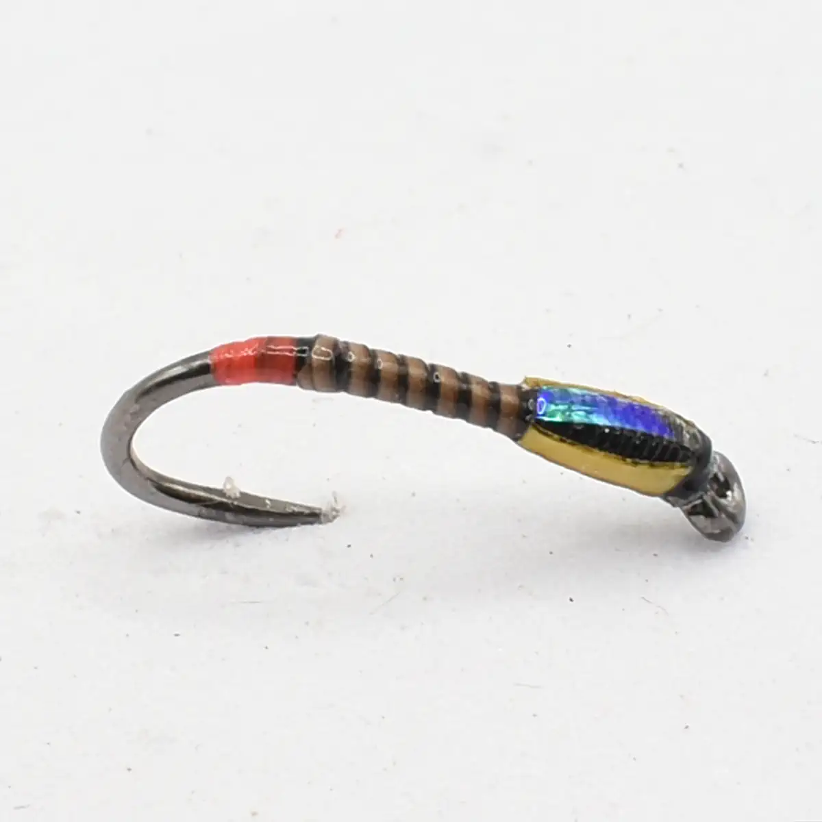 Single fishing hook with a small iridescent, multicolor lure body attached near the barb, lying on a white surface.