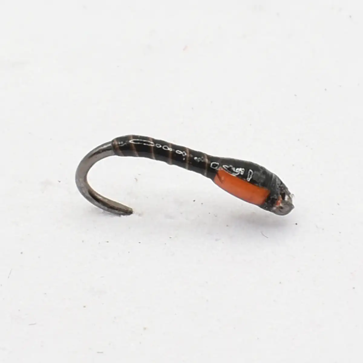 Small fishing hook with a black and red soft plastic lure attached, resting on a white surface.