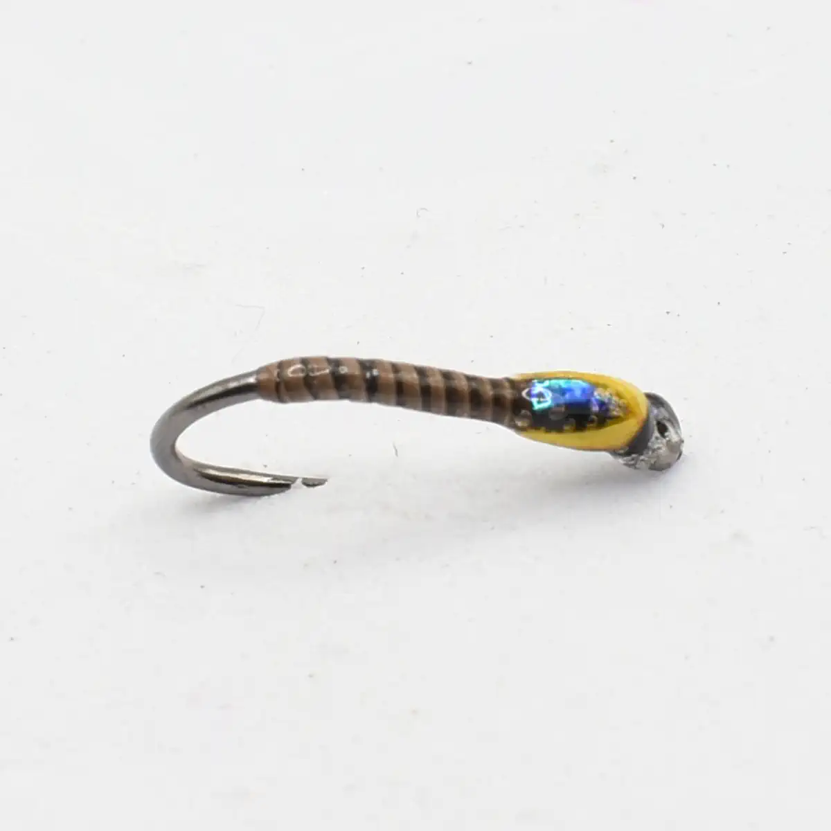 Artificial fishing lure with a brown striped body, yellow head, and a curved hook on the left; mimics a larva.