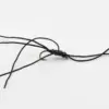 Tangled black cord bracelet with small black beads and a metal clasp on a white surface (jewelry in progress).