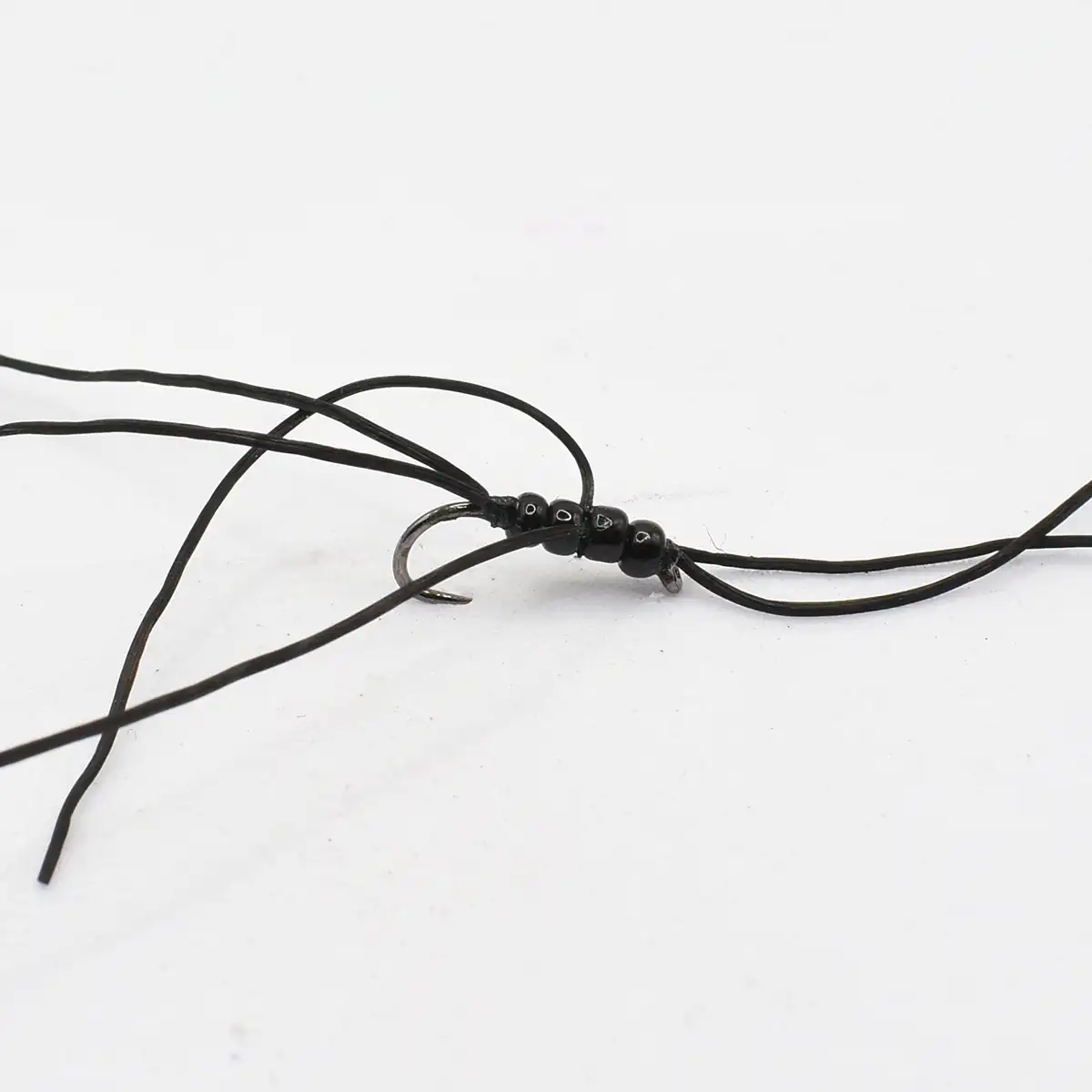 Tangled black cord bracelet with small black beads and a metal clasp on a white surface (jewelry in progress).