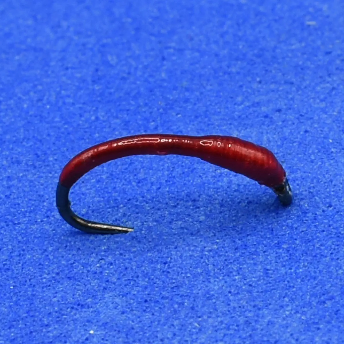 Red curved fishing hook with a black tip on a blue surface