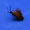 Close-up of a black fishing fly with orange hackle feathers on a blue background, showing the hook and body detail.