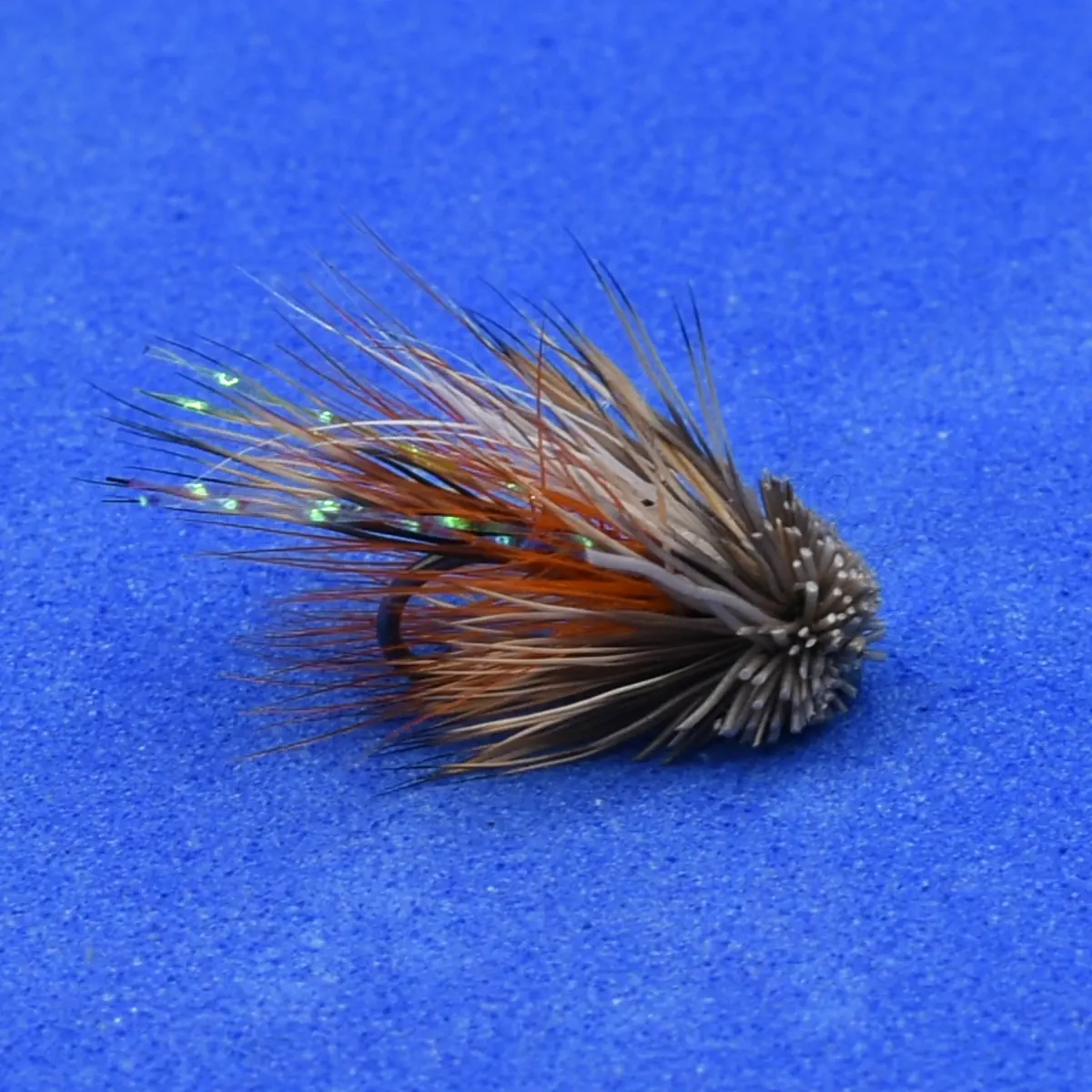 A close-up of a feathered fishing lure with brown, orange, and grey hairs on a blue background.