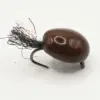Brown egg-shaped fishing lure with a curved hook and dark fiber tail, shown from the side with a small reflective dot on its surface.