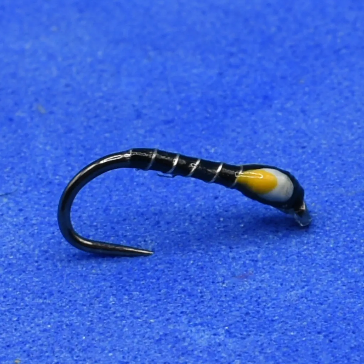 Close-up of a small fishing hook tied with black thread and a yellow bead lure against a blue background.