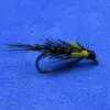 A black fishing fly lure with a curved hook, straw-colored body, and wispy tail on a blue background (angling fly)