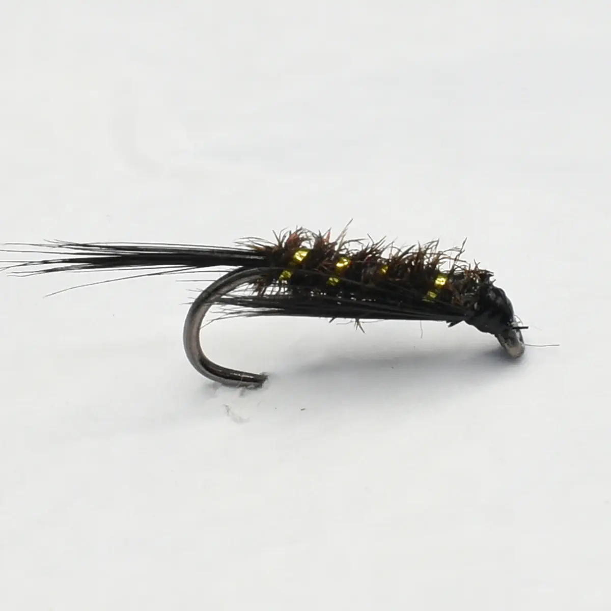 Close-up of a black, fuzzy fishing fly with a curved hook and small yellow bead accents, used as a fly fishing lure.