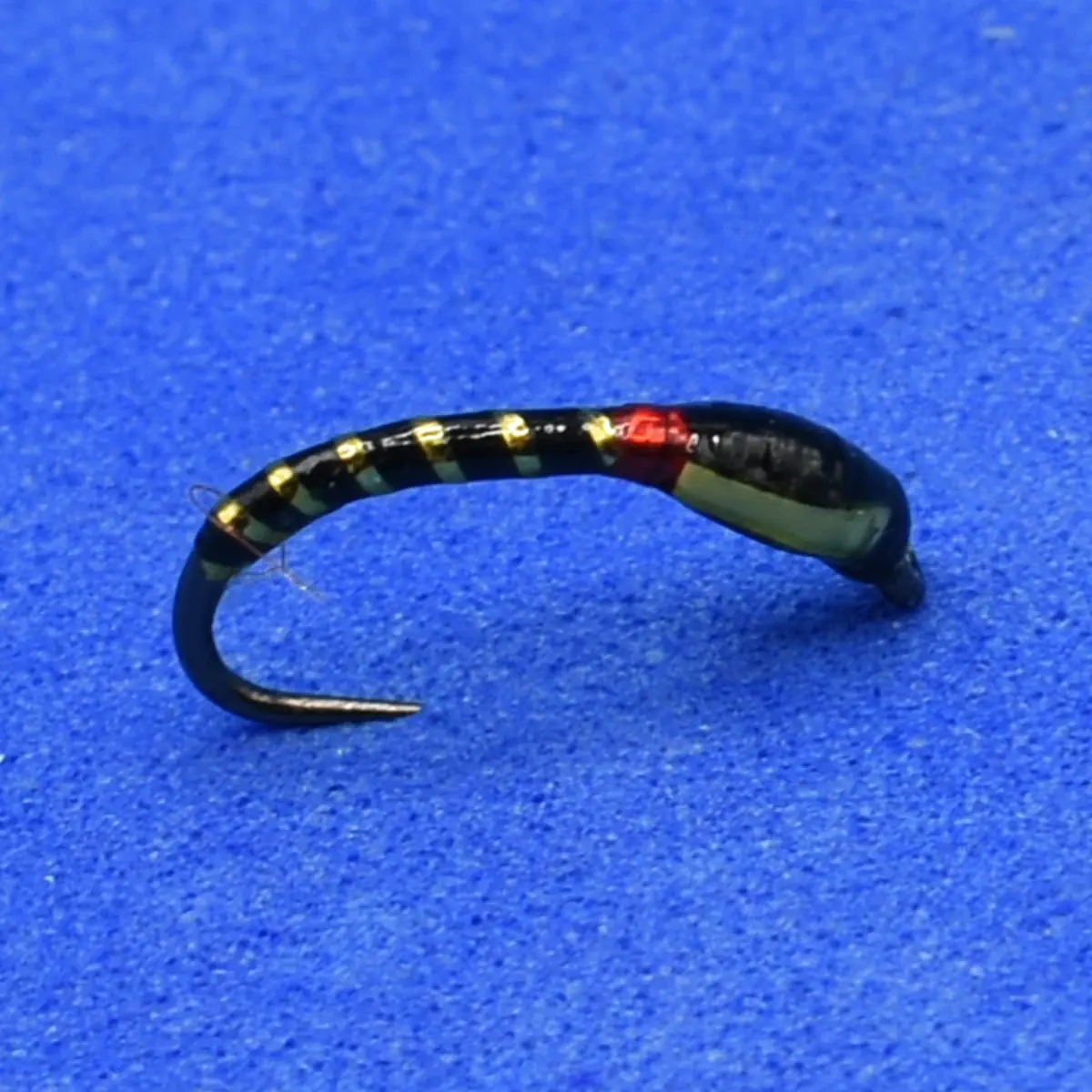 Close-up of a black fishing lure with gold beads along its body on a blue background.