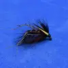Macro shot of a tied fishing fly with black hackle, yellow tag, and iridescent bead accents against a blue background.