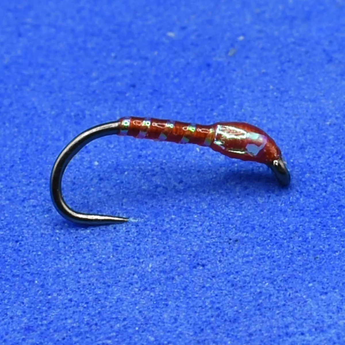 Close-up of a red-wrapped fishing jig attached to a curved hook on a blue background, ready for fishing.